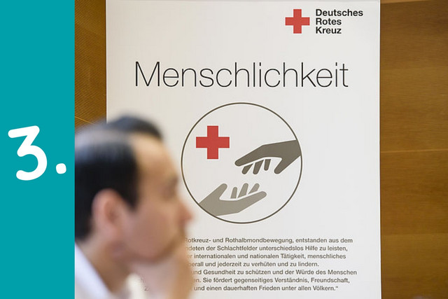 Eine Person sitzt in einer nachdenklichen Pose vor einem Aufsteller des Deutschen Roten Kreuzes.